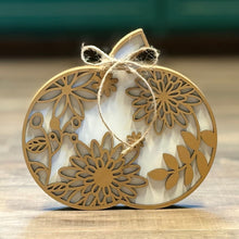Load image into Gallery viewer, A decorative autumn-themed wooden ornament shaped like a pumpkin, featuring laser-cut floral patterns and a natural jute twine bow, set on a wooden surface.
